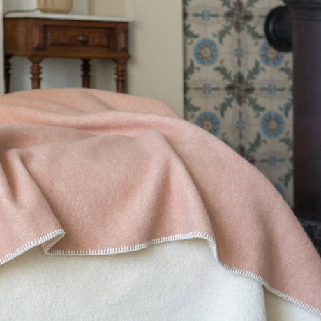 Wollen beddeken in zandkleur gebruikt als extra laag op bed in een rustige setting