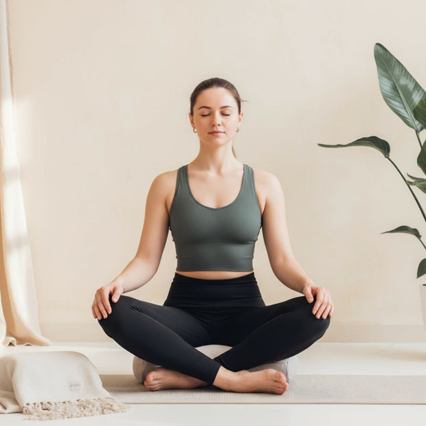 Vrouw mediteert ontspannen op een halve maan meditatiekussen met rechte rug en zachte uitstraling