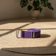 Een opgerolde acai-paarse katoenen yogariem met een stevige metalen D-ring gesp voor veilige ondersteuning tijdens yoga.