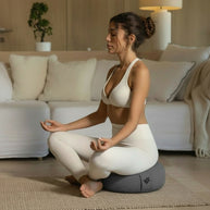 Vrouw mediteert ontspannen op een rond meditatiekussen in een rustige, lichte ruimte