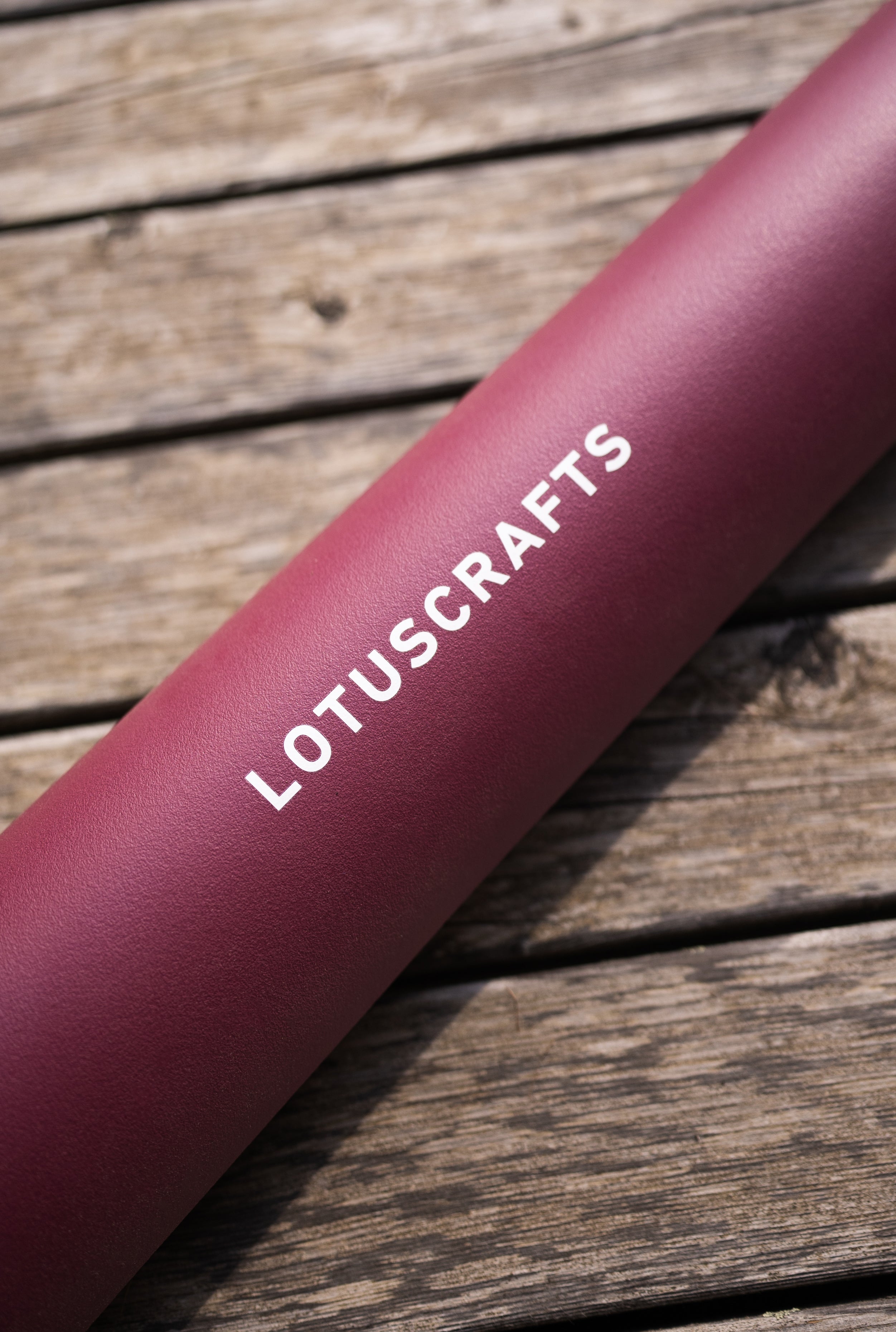 Detail van roze Arise Yogamat op houten ondergrond aubergine wijn rood